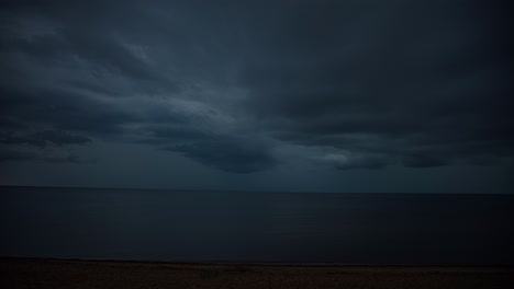 Static-view-of-dark-rain-clouds-passing-by-over-the-sea-in-timelapse-along-the-empty-sandy-beach