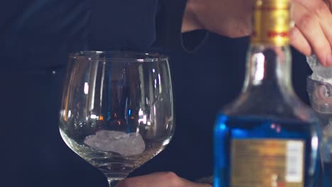 Adding-ice-to-a-glass-in-preparation-for-mixing-a-blue-cocktail---isolated-slow-motion