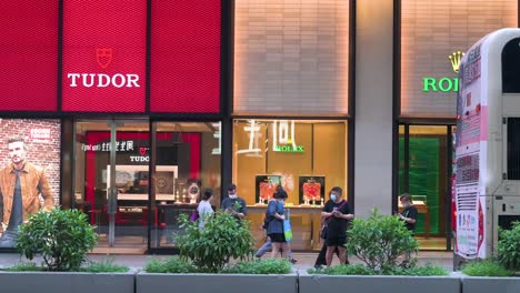 Chinese-commuters-and-pedestrians-walk-past-the-Swiss-high-end-watchmaker-manufacturers-and-brands-Tudor-and-Rolex-stores-while-traffic-drives-through-the-frame-in-Hong-Kong