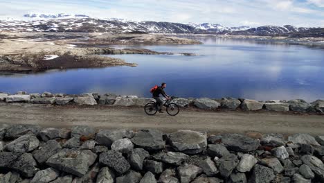 Aerial-Follow-Shot-Of-Male-Cycling-Across-Sysen-Dam-In-The-Municipality-Of-Eidfjord-in-Hordaland,-Norway