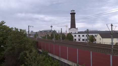 A-commuter-train-on-the-way-to-Aachen-in-Cologne-Ehrenfeld-on-a-cloudy-day-in-front-of-the-panorama-scenery-of-Cologne-Ehrenfeld-with-the-TV-tower-in-the-background