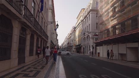 Tourist-and-locals-walk-down-historic-streets-of-Lisbon-inner-city-during-low-sunset,-Portugal