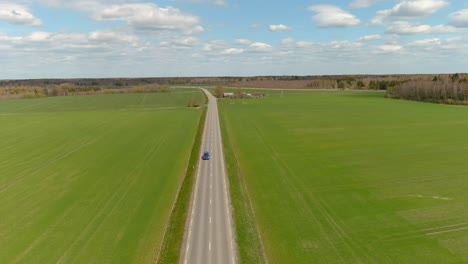 aerial-drone-view-of-rural-road-with-cars-moving-on-the-right-and-left-in-the-form-of-green-fields-in-Lithuania