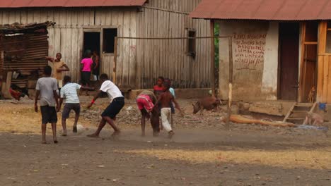 Niños-Jugando-Al-Fútbol-Frente-A-Las-Casas-En-Ruinas-En-Un-Pueblo-Pobre-En-África---Toma-Amplia