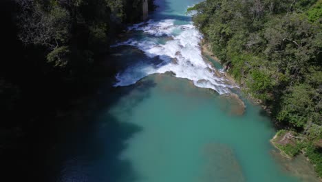 Flying-backward-from-a-bridge-that-cross-a-turquoise-water-river-in-the-middle-of-the-jungle-of-Chiapas,-Mexico