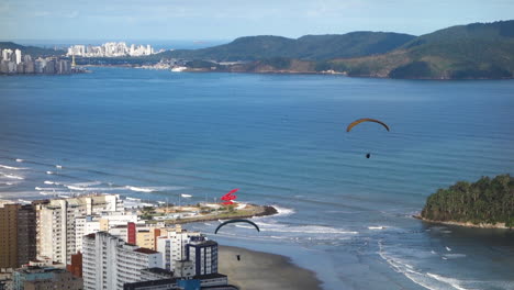 Gleitschirme-Mit-Fallschirmen,-Die-über-Santos,-Brasilienstrand-Und-Gebäuden-Am-Wasser-Fliegen