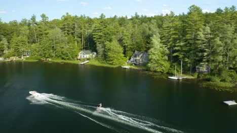 Aerial-drone-following-shot-over-a-motor-boat-pulling-a-water-skier-on-a-bright-sunny-day-in-Sunset-lake-in-New-Hampshire,-USA
