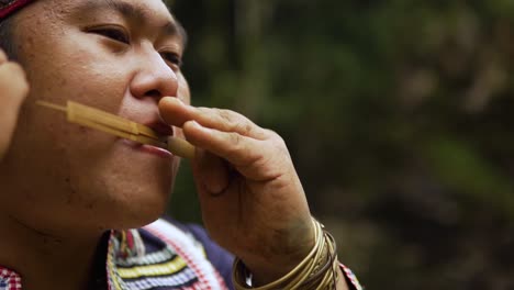 Primer-Plano-De-Un-Indígena-Tocando-El-Instrumento-Tribal-Kubing,-Detrás-Hay-Una-Cascada