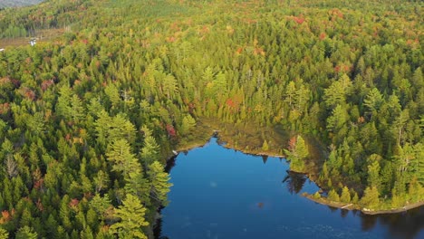 Aerial-drone-orbiting-around-a-bright-blue-lake-with-colorful-autumn-trees-surrounding-the-water-as-summer-ends-and-the-seasons-change-to-fall-in-Maine