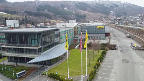 Nordan-factory-facilities-and-flags-in-Moi-Norway---Aerial-ascending-in-front-of-waving-flags-before-revealing-panoramic-factory-view---Window-and-doors-factory