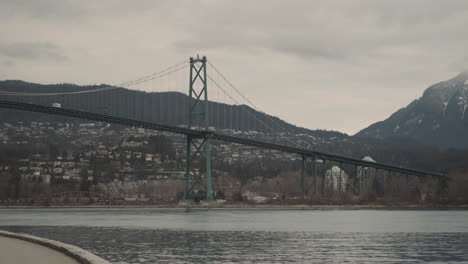 Wide-panning-shot-of-Lions-Gate-bridge-and-snow-packed-mountains-on-cloudy-morning