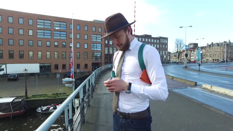 An-elegant-man-in-dandy-style-with-white-shirt-and-beard-makes-a-phone-call-on-the-Kadijksplein-bridge-in-Amsterdam