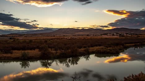 Time-lapse-of-a-cloudscape-reflecting-off-a-glassy-river-at-sunset-with-mountains-in-the-distance