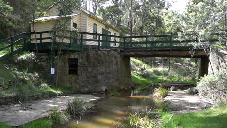 Gimble-shot-of-an-old-wooden-and-stone-bridge-over-a-stream-or-creek,-next-to-a-weatherboard-shed-in-the-Australian-bush