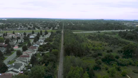 Aerial-Footage-Over-Small-Sub-Division-and-Forest-with-a-Train-Track-in-The-Middle-in-The-Evening