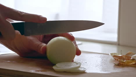 A-close-up-of-slicing-an-onion-with-a-knife-on-a-wooden-board