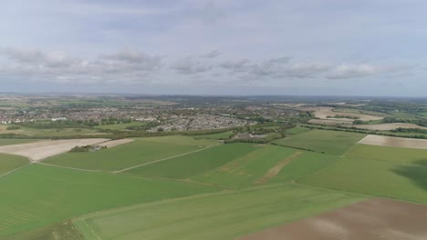 Wide-aerial-tracking-forward-toward-the-town-of-Poundbury,-just-outside-of-Dorchester,-Summer-weather,-fields-are-vibrant