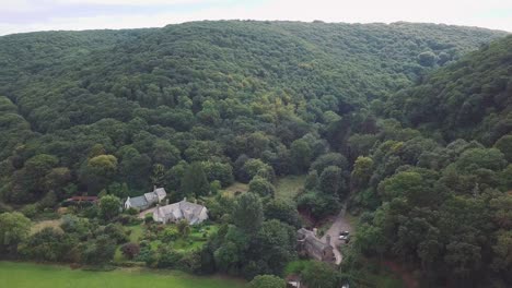 Aerial-tracking-forward-from-the-coastline-over-the-fields-and-forests-on-the-edge-of-Exmoor,-Manor-or-country-house-in-the-foreground