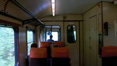 Looking-through-the-front-windows-of-an-old-orange-train---railcar-that-are-moving,-with-people-in-the-foreground
