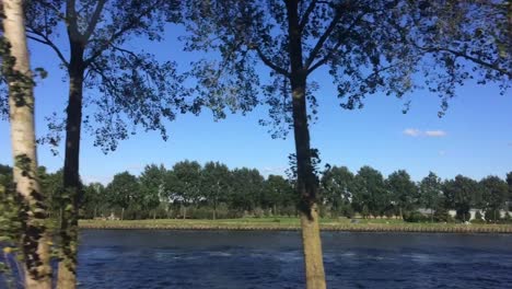 Siguiendo-Parte-Del-Canal-De-Amsterdam-En-Los-Países-Bajos-Con-Un-Barco-Que-Pasa-Por-El-Canal-Permaneciendo-En-El-Mismo-Nivel-Que-El-Agua
