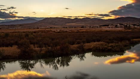 Time-lapse-of-a-beautiful-sunset-with-a-cloudscape-reflecting-off-the-smooth-surface-of-a-river-and-mountains-in-the-background---panning-left