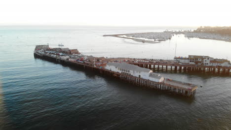 Aerial-drone-shot-of-Stearns-Wharf-pier-and-sailboats-in-the-Pacific-ocean-sailing-into-the-Santa-Barbara-Harbor,-California