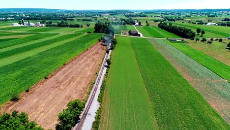 Steam-Train-Passing-through-Amish-Farm-Lands-and-Countryside-on-a-Sunny-Summer-Day-as-seen-by-Drone