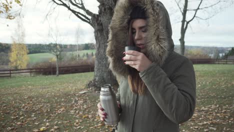 Adult-girl-is-pouring-her-warm-drink-and-drinking-it-on-cold-autumn-day