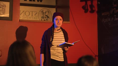 Young-women-reads-slam-poetry-book-and-walks-off-stage-wearing-red-beanie