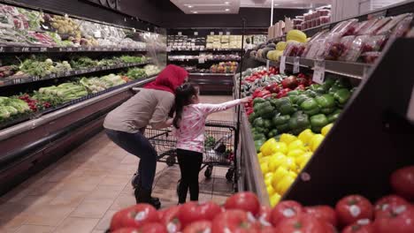 Mother-and-daughter-walking-through-a-grocery-store-picking-red-peppers