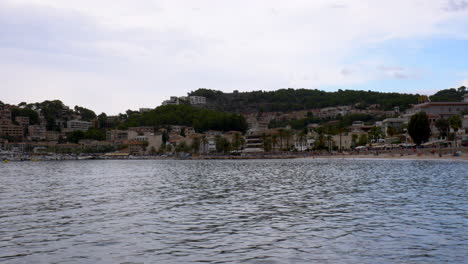 The-beach-of-Port-D’Sóller,-Mallorca,-seen-from-the-pier-with-the-city-and-mountains-in-the-background