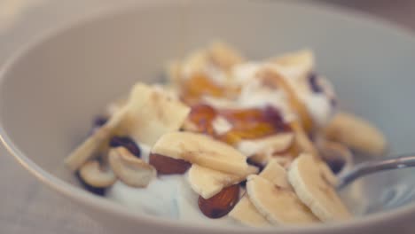 Honey-being-drizzled-over-a-bowl-of-Greek-yoghurt,-nuts-and-bananas