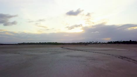 Drone-flying-low,-fast-and-straight-over-winding-animal-tracks-on-large-mud-flats-and-then-rising-to-reveal-beautiful-cloudy-sunset