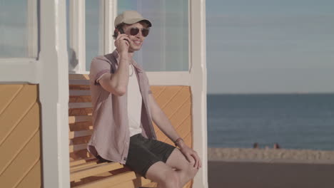 A-Man-Sat-On-A-Bench-On-The-Beach-Receives-A-Call-From-A-Good-Friend