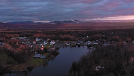 Aerial-footage-flying-backwards-away-from-small-community-on-shore-of-lake-at-sunrise-in-late-fall-with-misty-mountains-in-the-background