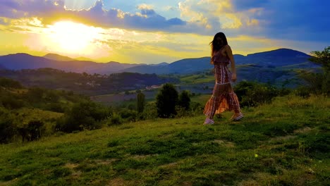 Sunset-over-the-mountains-with-a-girl-dancing-and-spinning-in-joy-on-a-grassy-hill