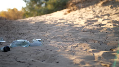Low-slide-shot-of-a-broken-bottle,-trash-and-litter-on-a-natural-dirt-hiking-trail-at-sunrise