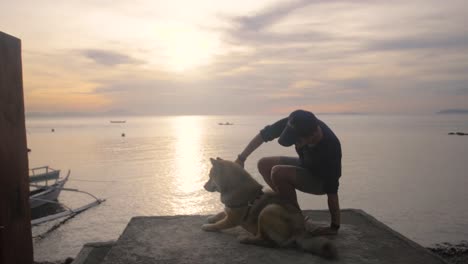 Zeitlupenvideo-Eines-Mannes,-Der-Einen-Hund-Auf-Einer-Plattform-Umarmt,-Mit-Sonnenuntergang-Im-Hintergrund