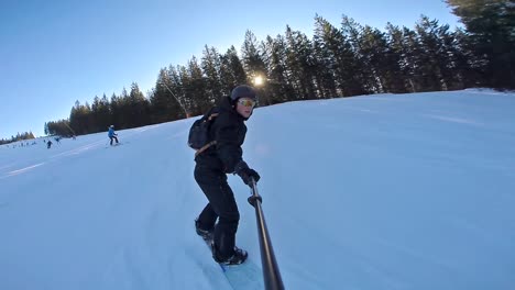 Front-action-cam-view-of-a-high-speed-snowboarder-with-selfie-stick-in-the-evening,-60-fps