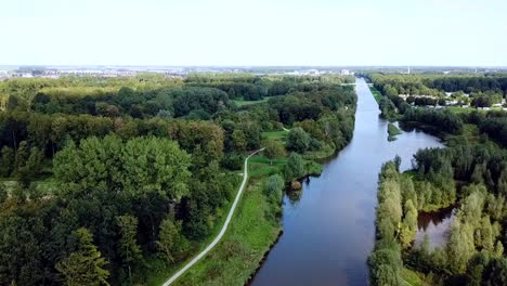 Drohne-Fliegt-über-Den-Kanal-Im-Wald-Mit-Einem-Dorf-Im-Hintergrund