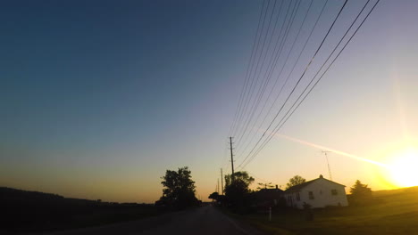 Car-driving-through-a-farming-community-at-sunset