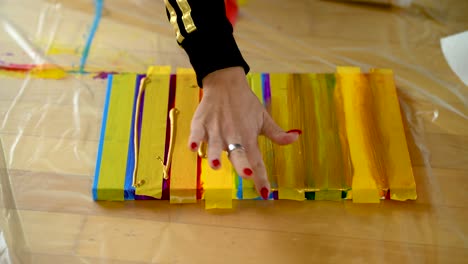 A-woman-using-painters-tape-to-finish-her-colorful-stripes-on-a-canvas