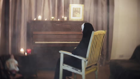 Spooky-creepy-Nun-in-a-horror-scene,-rocking-in-a-rocking-chair-in-a-living-room-with-a-piano,-a-doll-and-candles
