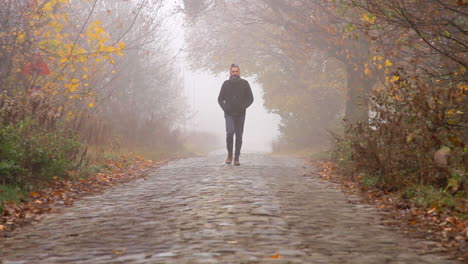 A-man-is-walking-towards-the-camera-on-a-stone-paved-road-during-a-foggy-misty-morning