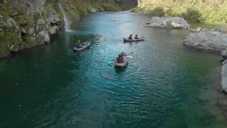 SLOWMO---People-on-kayak-trip-paddle-boats-through-canyon-on-Pelorus-river,-New-Zealand-with-native-forrest-and-rock-boulders---Aerial-Drone