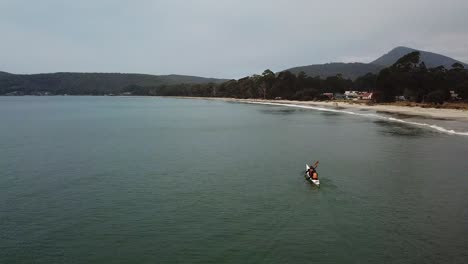 Drone-View-Of-Person-In-Kayak-Paddling-In-Clear-Aqua-Water-Along-Beach,-Bruny-Island,-Tasmania,-Australia
