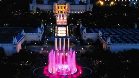 Aerial-view,-fountains-of-Monjuic-colorfull-at-night-from-above,-revealing-the-city,-Barcelona,-Spain