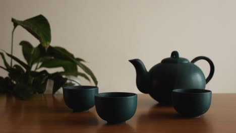 Minimaler-Hintergrund-Eines-Grünen-Japanischen-Teesets-Mit-Dampf-Aus-Den-Tassen,-Auf-Einem-Holztisch,-Mit-Einer-Pflanze-Im-Rücken