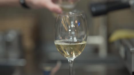 Die-Männlichen-Hände-Gießen-Eine-Flasche-Weißwein-Champagner-In-Transparentes,-Sauberes-Rundes-Glas-Auf-Dem-Resraurant-Tisch-In-Verschwommenem-Nahkonzept