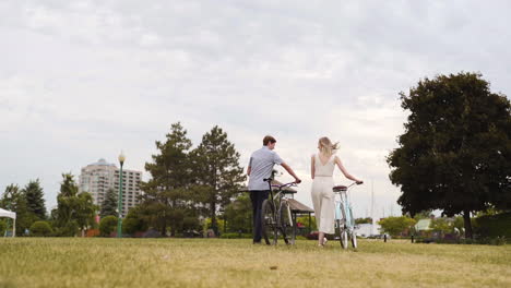 Attraktives-Junges-Paar,-Das-Seine-Fahrräder-In-Einem-Park-In-Zeitlupe-Spaziert